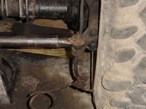 1992 Ford Bronco - Close-up of a rusty tie rod end and steering linkage connected to a vehicle's wheel hub.