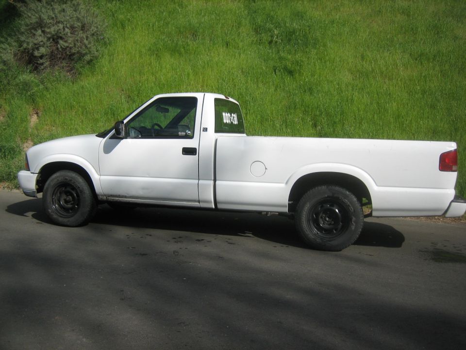 White pickup truck, side view, parked on asphalt with grassy hill in background