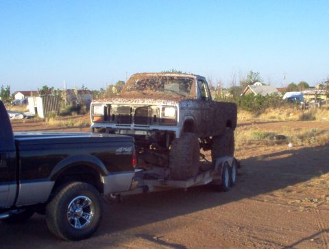 1995 Ford Bronco - A heavily mud-caked pickup truck is loaded onto a trailer, with another truck visible in the foreground.