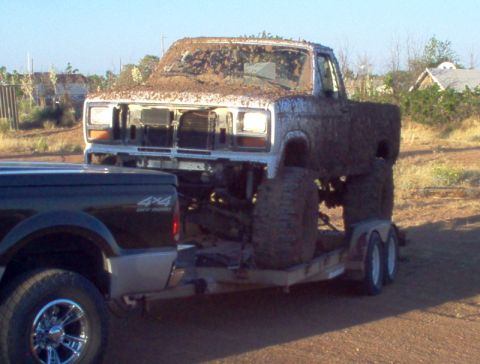 1995 Ford Bronco - A heavily mud-covered pickup truck is transported on a trailer, with another truck visible in the foreground.