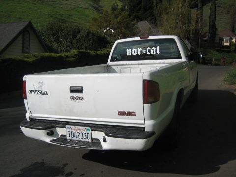 1995 Ford Bronco - White GMC pickup truck parked on a paved road with houses and trees in the background.