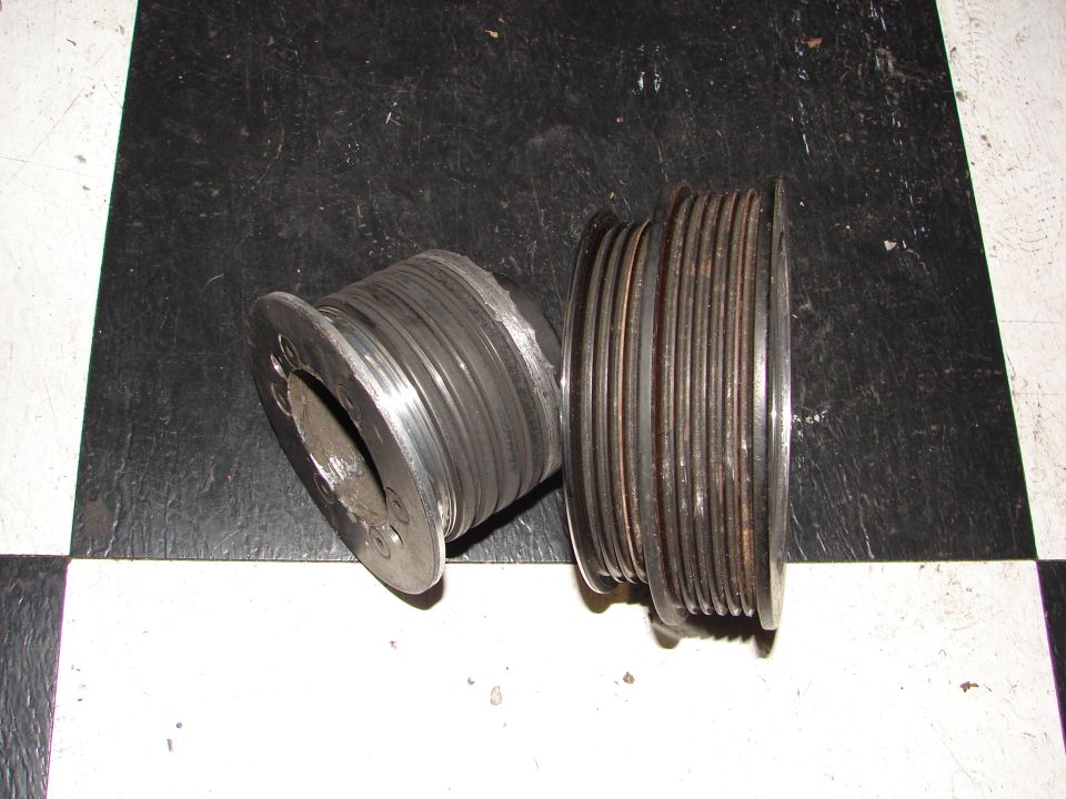 Two metal pulleys with grooves, one worn, on a checkered surface