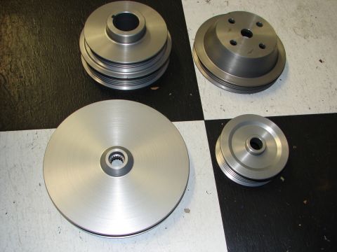 1992 Ford Taurus - A set of four metal pulleys, including a large single-groove pulley and a smaller multi-groove pulley, are displayed on a checkered surface.