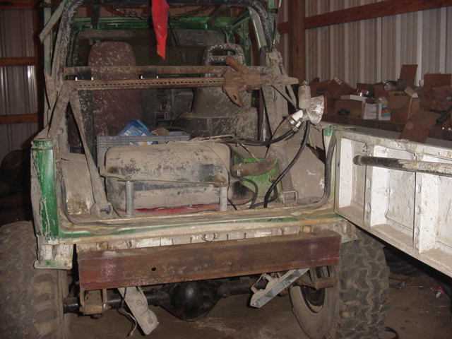 Stripped green vehicle tub with roll cage and exposed rear interior inside a metal shop