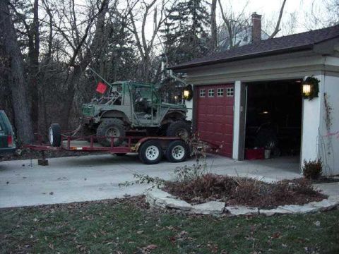 1992 Ford Bronco - An off-road vehicle with a roll cage and large tires is loaded onto a trailer next to a garage.