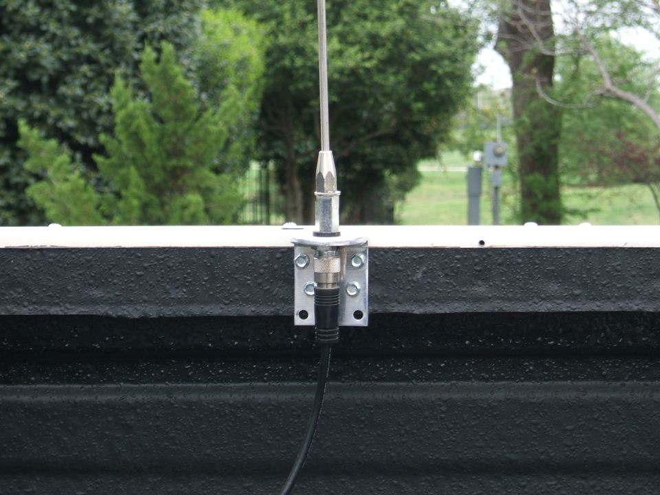 Antenna mount on textured black surface with trees in background