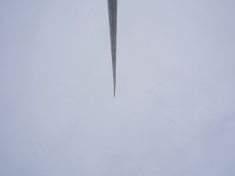 1991 Ford Bronco - Close-up of a thin tapered antenna whip photographed against a flat overcast sky, with no other subject in frame. The metal rod narrows to…