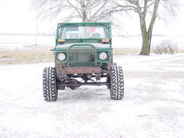 Green off-road vehicle with large tires and a brush guard, front view in a snowy field