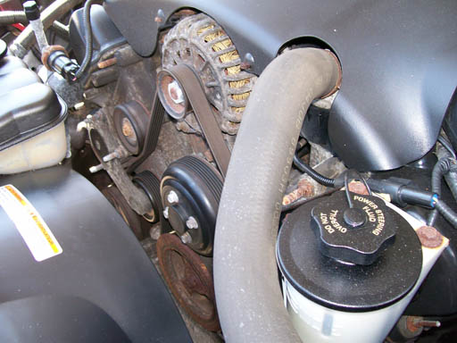 Engine bay with power steering fluid reservoir, hoses, belts, and pulleys visible