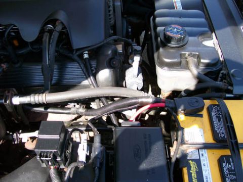 1999 Ford Crown Victoria - Close-up view of a vehicle's engine bay, showing the coolant reservoir, battery, and fuse box with a Ford logo.