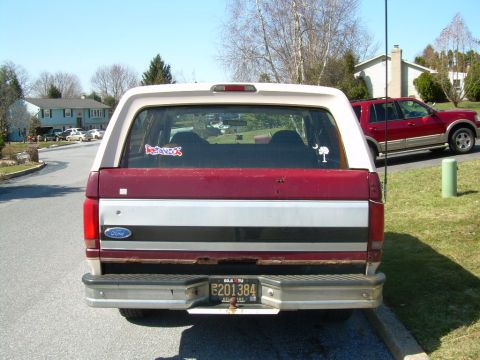 1992 Ford Bronco - The rear of a red and white 1992 Ford Bronco is visible, with a red SUV in the background.