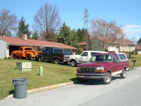 1992 Ford Bronco - A red 1992 Ford Bronco is parked on the street in front of a house, with other vehicles visible in the driveway.