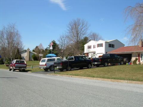 1992 Ford Bronco - Multiple Ford vehicles, including a Bronco and pickup trucks, are parked in a suburban driveway on a sunny day.