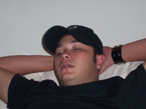 1997 Ford Crown Victoria - A man in a black baseball cap and t-shirt rests with his hands behind his head, showing visible text on his shirt.