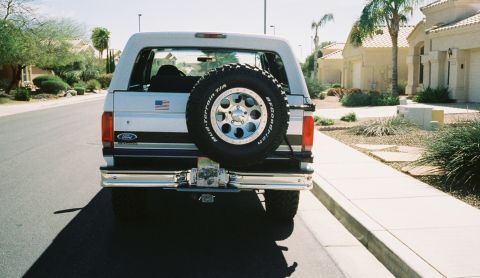 1996 Ford Bronco - Rear view of a white 1996 Ford Bronco, a spare tire mounted on the tailgate and an American flag decal.