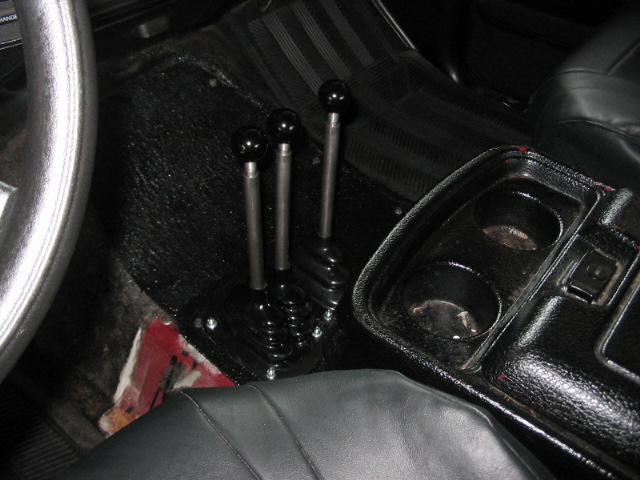 Interior view of a vehicle showing three manual shifters and a center console with cup holders