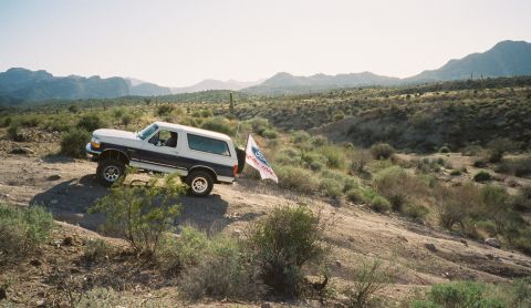 1996 Ford Bronco - A two-tone Ford Bronco navigates a dusty desert trail under a bright sky.
