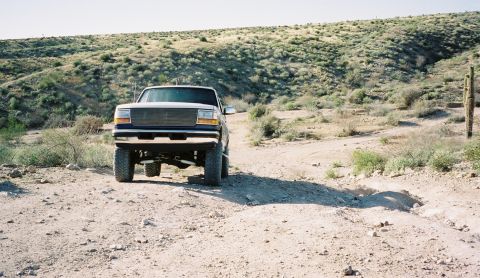 1996 Ford Bronco - A blue pickup truck navigates a dusty desert trail under a clear sky.