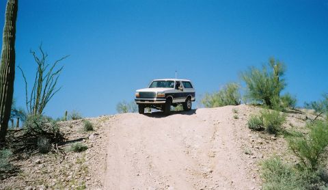 1996 Ford Bronco - A two-tone Ford Bronco navigates a dusty incline under a clear blue sky.