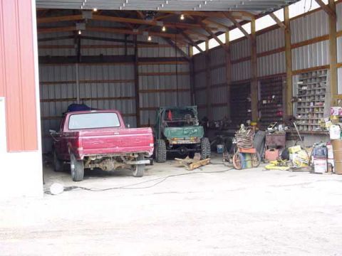 1992 Ford Bronco - Two vehicles, a red pickup and a green off-road vehicle, are stored inside a barn.