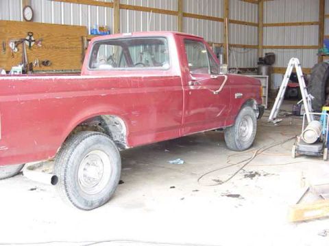 1992 Ford Bronco - A red pickup truck sits in a garage with tools and equipment around it.