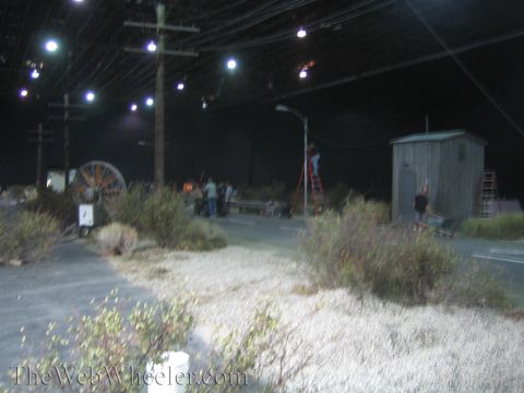 1990 Ford Bronco - Indoor film set dressed as a dimly lit street at night, with overhead lights, utility poles, a large cable reel and a shed.