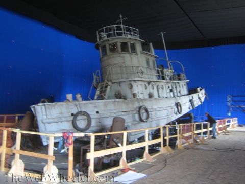 1990 Ford Bronco - Weathered gray tugboat prop mounted on a motion base against a blue screen, encircled by a wooden safety railing.
