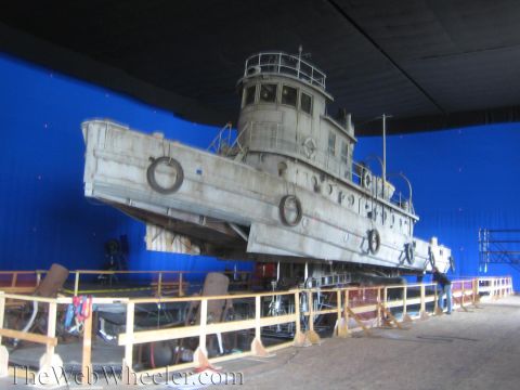 1990 Ford Bronco - Gray tugboat prop tilted on a soundstage motion rig in front of a blue screen, with a worker visible at the right.
