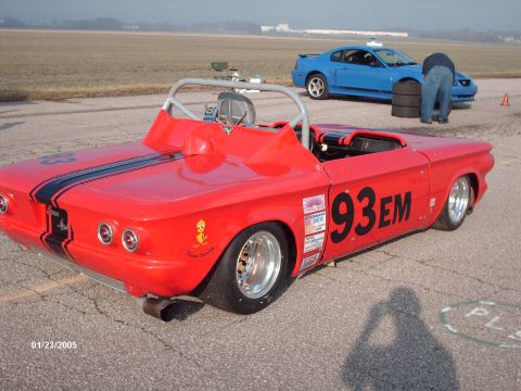 1995 Ford Probe - A red custom race car with racing decals and stripes is parked on asphalt, with a blue Ford Mustang in the background.