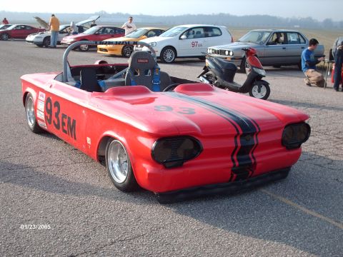 1995 Ford Probe - A red convertible race car with racing stripes and the number 93 is parked on asphalt with other vehicles in the background.