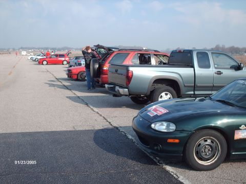 1995 Ford Probe - Multiple vehicles are parked on an asphalt lot, with a person attending to one of the cars.
