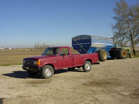 1992 Ford Bronco - A red pickup truck tows a large blue trailer, with a tractor visible in the background.