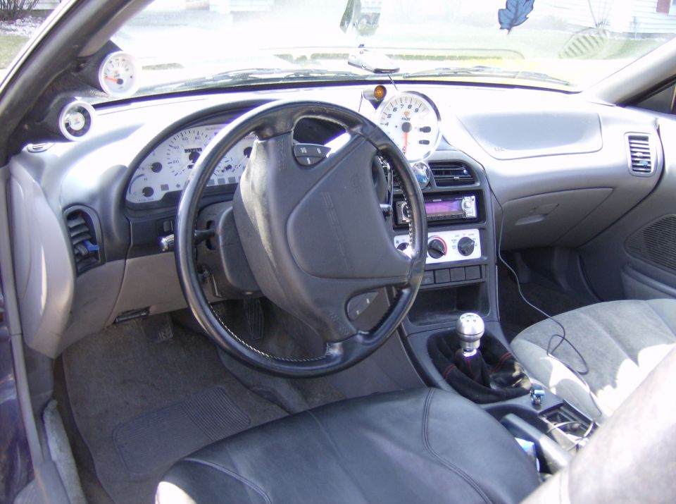 Interior shot of a car, showing the steering wheel, dashboard gauges, and center console with a manual shifter