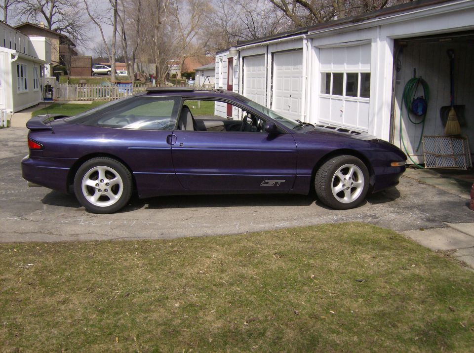 Purple sport coupe in side profile parked by a white garage