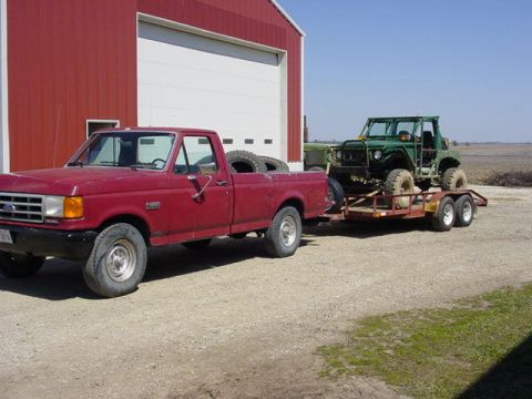 1992 Ford Bronco - A red 1992 Ford F-250 pickup truck is parked in front of a red barn, towing a green off-road vehicle on a trailer.