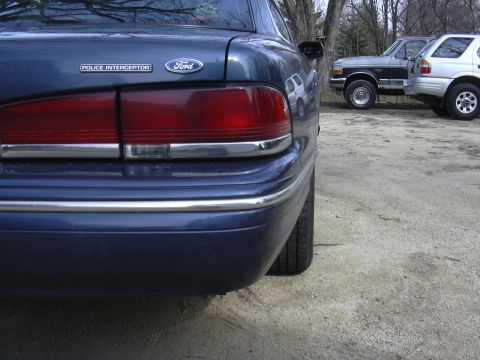 1996 Ford Crown Victoria - The rear quarter panel and taillight of a blue Ford Crown Victoria Police Interceptor are visible, parked next to other vehicles.