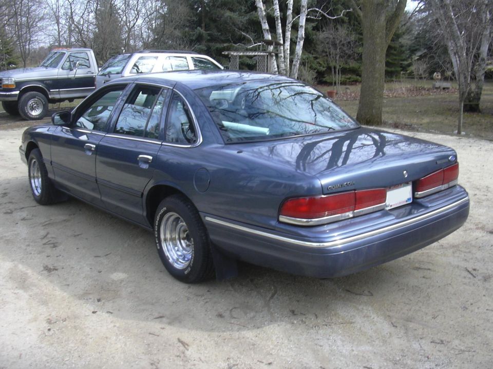 Blue Ford Crown Victoria rear three-quarter view on gravel with polished wheels