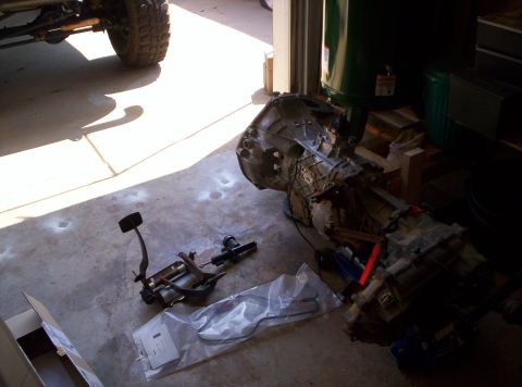 1995 Ford Bronco - A transmission and brake pedal assembly are laid out on a concrete floor, possibly for repair or replacement.