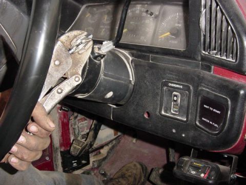 1992 Ford Bronco - A hand grips vice grips clamped onto the steering column of a 1992 Ford F-250, with the dashboard and gauges in view.