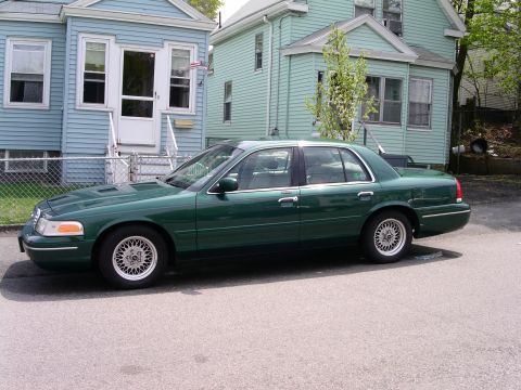 2001 Ford Crown Victoria - A green 2001 Ford Crown Victoria sedan is parked on a street in front of two houses.