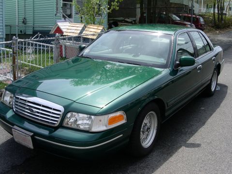 2001 Ford Crown Victoria - A green 2001 Ford Crown Victoria sedan is parked on a street, showing its front and side profile.