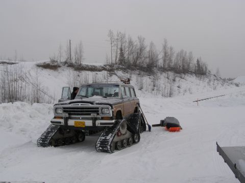 2000 Ford E350 - A Jeep Grand Wagoneer is equipped with tracks for snow travel, with the driver's door ajar.
