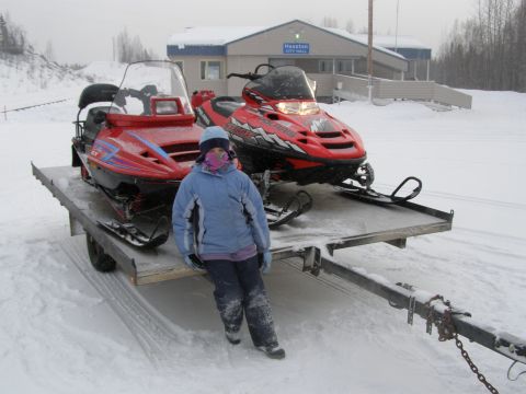 2000 Ford E350 - A person stands next to two snowmobiles loaded onto a trailer in a snowy environment.