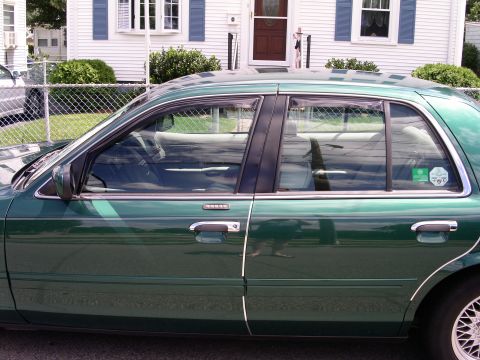 2001 Ford Crown Victoria - Side view of a green 2001 Ford Crown Victoria sedan parked in front of a house.