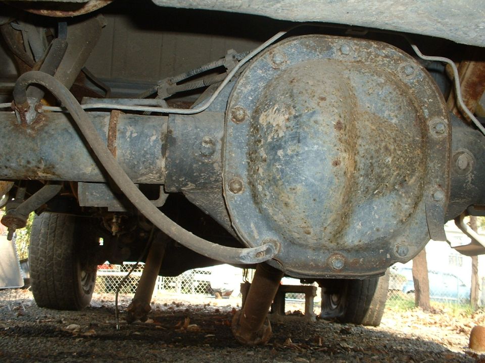 Underside view of a rusty solid axle and differential cover with disconnected driveshaft on a 4x4