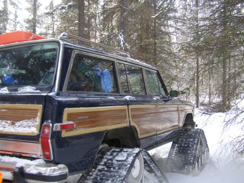 2000 Ford E350 - A dark blue Jeep Grand Wagoneer with wood paneling is equipped with snow tracks for traversing a winter forest.