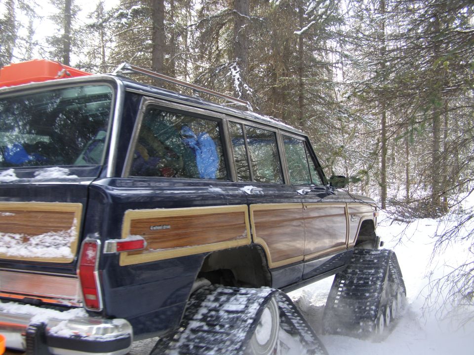 Dark blue Jeep Grand Wagoneer with wood paneling on snow tracks in a snowy forest