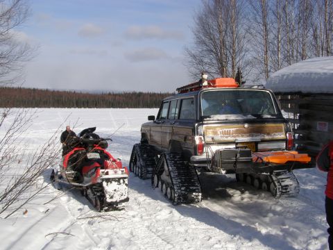 2000 Ford E350 - A Jeep Grand Wagoneer equipped with tracks sits in the snow beside a snowmobile.