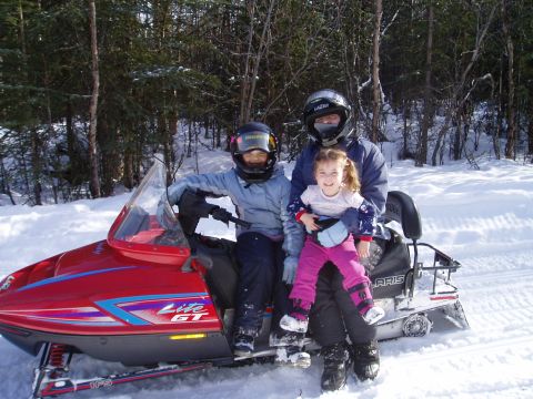 2000 Ford E350 - A family enjoys a ride on a red snowmobile in a snowy, wooded area.