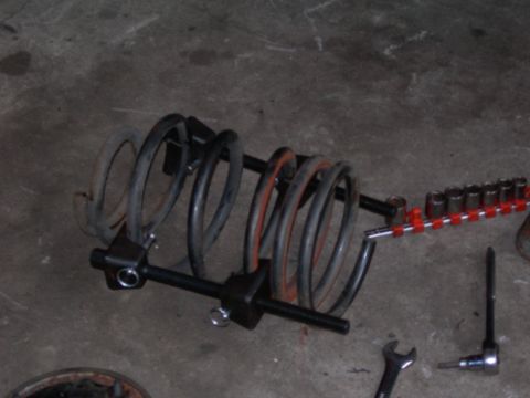 1992 Ford Taurus - A spring compressor tool is shown with a coil spring and a set of sockets on a concrete floor.